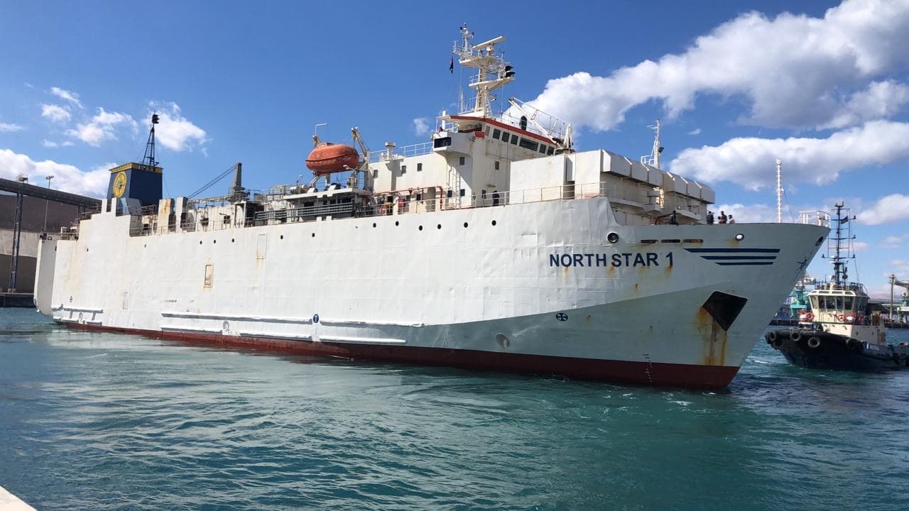 Large white vessel named North Star 1 on blue water under a bright cloudy sky.