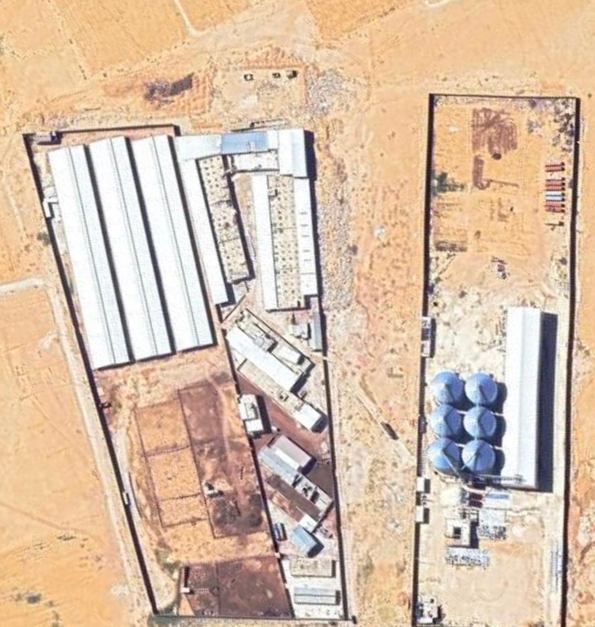 Satellite view of a large desert farm with white buildings, animal pens, and blue silos.