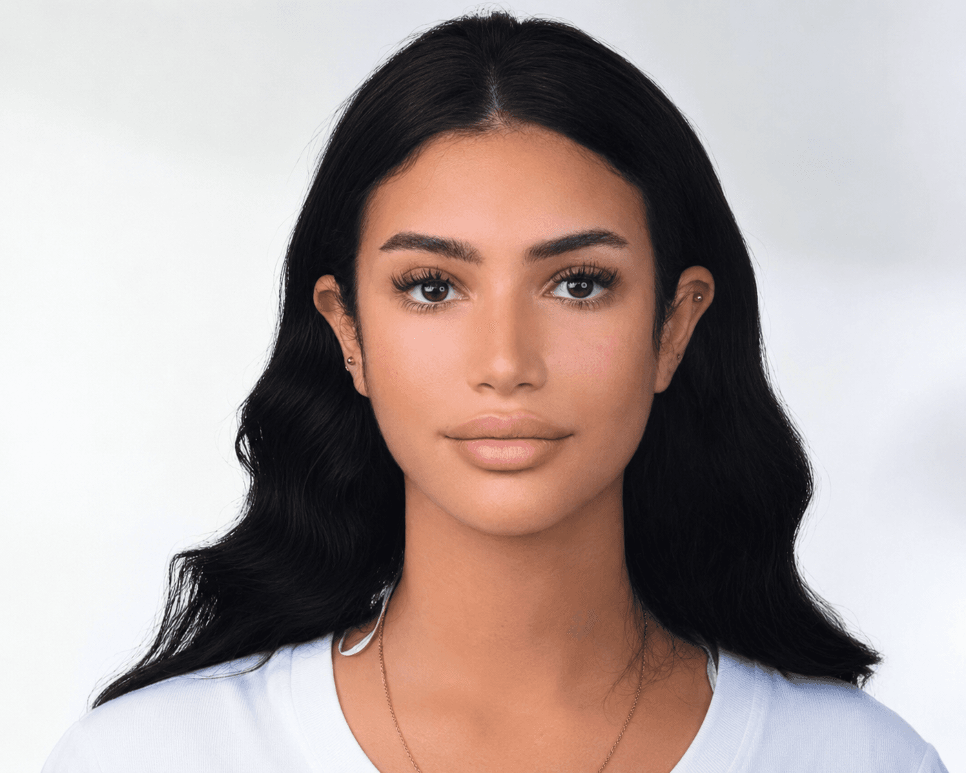 Portrait of a woman with long wavy black hair and brown eyes against white background.