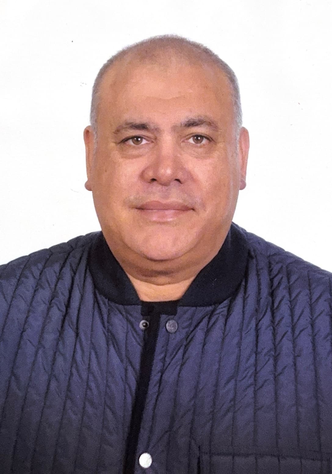 Smiling man with bald head, brown eyes, wearing a navy quilted jacket.